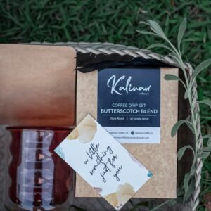 Flat lay of a Kalinew coffee drip set and accessories in a woven basket outdoors.